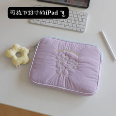 A light purple quilted tablet sleeve featuring embroidered flowers and a yellow flower-shaped keychain.