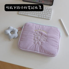A light purple, rectangular, embroidered laptop sleeve with a flower-shaped charm attached.