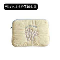 A light yellow quilted laptop sleeve featuring embroidered purple flowers and the text Two Flowers.