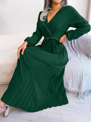 A woman wears a long-sleeved, dark green pleated maxi dress with a V-neck and a tie waist.