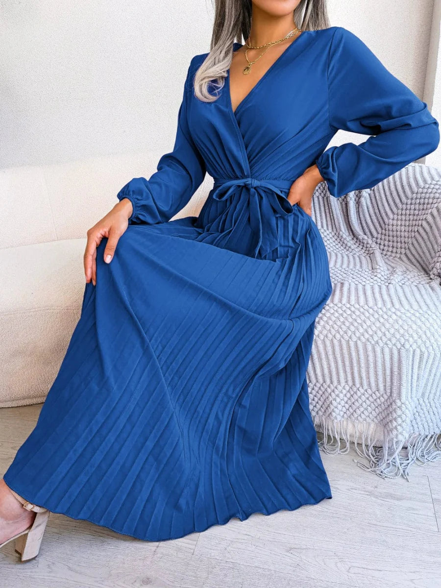 A woman wears a long-sleeved, royal blue pleated maxi dress with a V-neck and a tie waist.