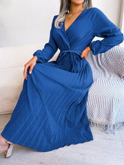 A woman wears a long-sleeved, royal blue pleated maxi dress with a V-neck and a tie waist.
