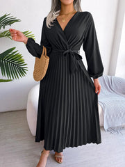 A woman wears a black long-sleeved maxi dress with a V-neck, a tie waist, and a pleated skirt.