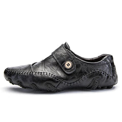 A black leather slip-on loafer with decorative stitching and a side button detail.