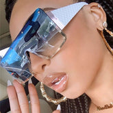 A woman wears oversized, one-piece rimless sunglasses with a blue gradient lens and white temples.