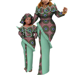A woman and a young girl wear matching African wax print dresses with long sleeves and ruffles.