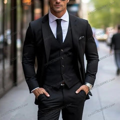 A man wears a formal black three-piece suit consisting of a blazer, vest, and trousers.