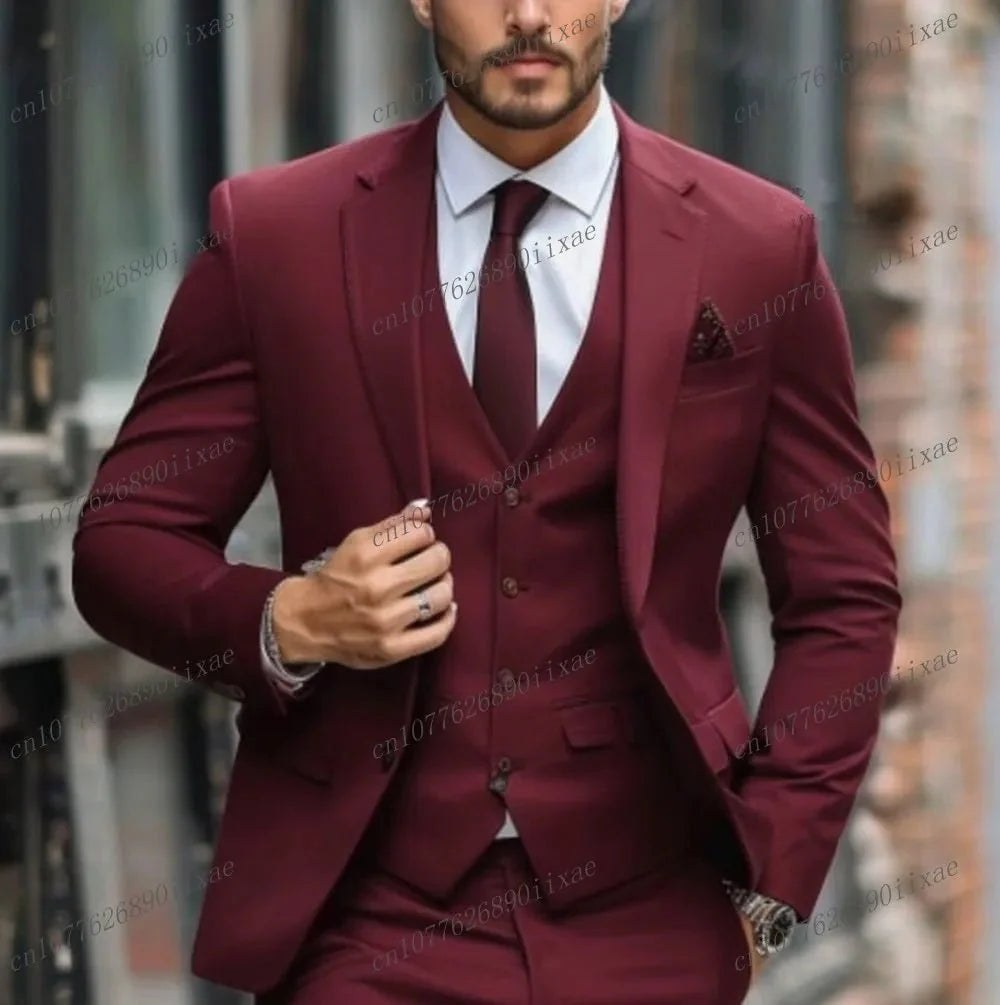A man wears a formal three-piece burgundy suit consisting of a blazer, vest, and matching trousers.
