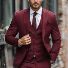 A man wears a formal three-piece burgundy suit consisting of a blazer, vest, and matching trousers.