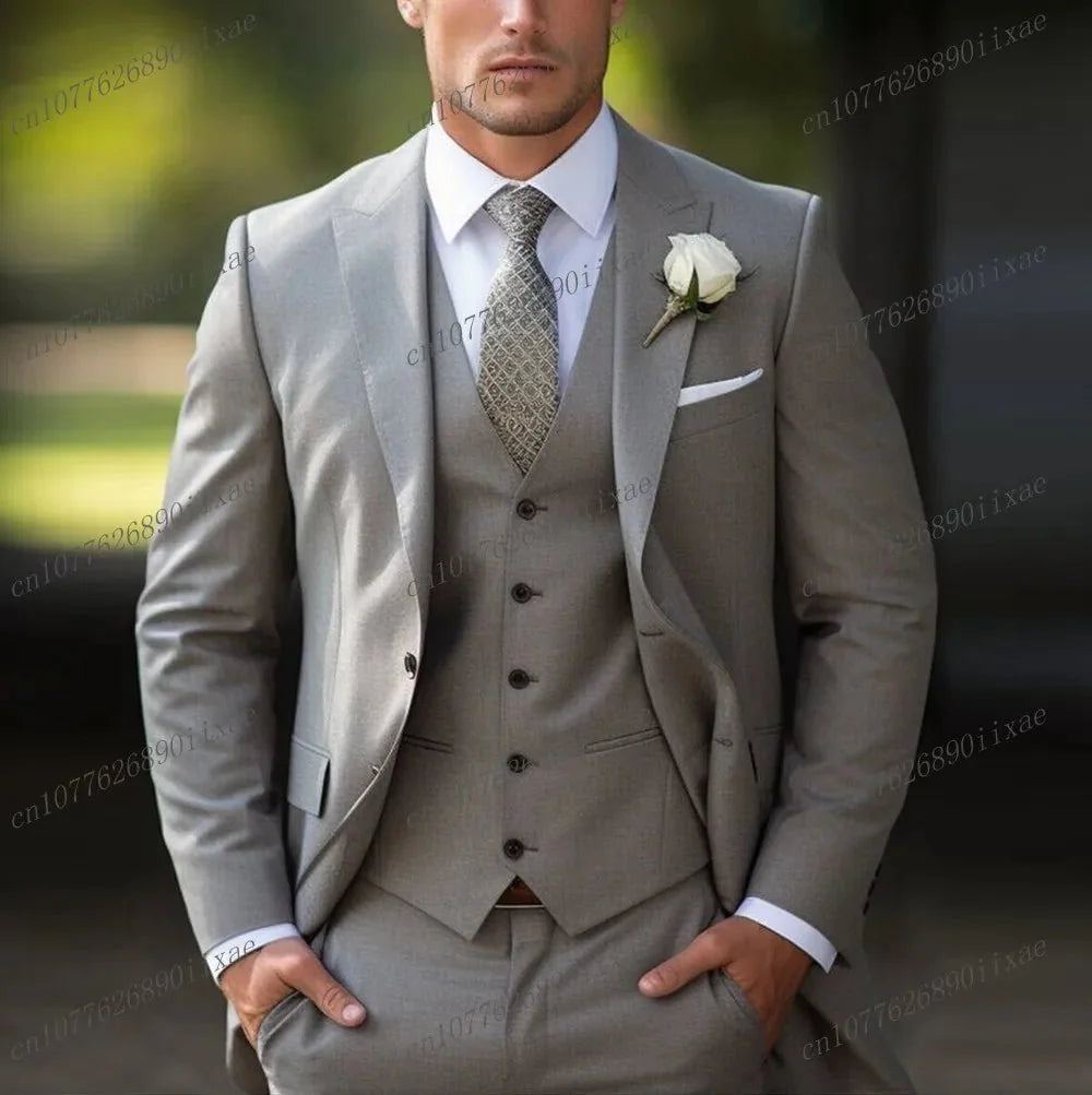 A man wears a formal light grey three-piece suit with a white shirt, patterned tie, and boutonniere.
