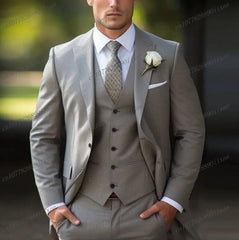 A man wears a formal light grey three-piece suit with a white shirt, patterned tie, and boutonniere.