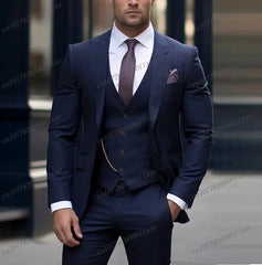 A man wears a formal navy blue three-piece suit with a white shirt and a patterned tie.