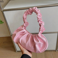 A soft pink, pleated hobo-style handbag with a gathered handle held in a hand.