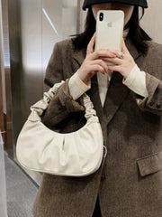 A woman holds a white, pleated, crescent-shaped shoulder bag with a gathered handle.
