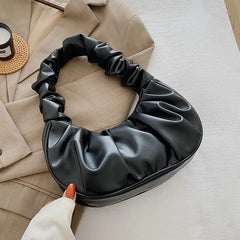 A black pleated hobo-style shoulder bag with a gathered handle resting on a beige blazer.