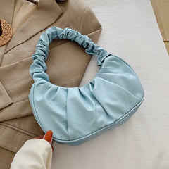 A light blue pleated hobo bag with a gathered handle held against a tan blazer.