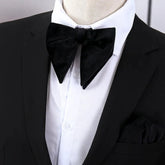 A large black velvet bow tie worn with a white dress shirt and a black suit jacket.