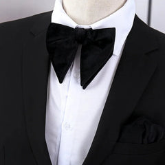 A large black velvet bow tie worn with a white dress shirt and a black suit jacket.