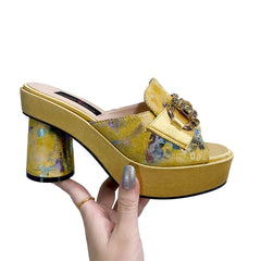 A gold platform mule with a round block heel, featuring a printed upper and a rhinestone buckle.