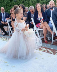 A young girl wears a floor-length tulle ball gown with long lace sleeves and floral appliques.