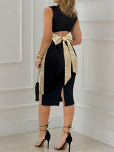 A woman wears a black sleeveless midi dress featuring a large gold sequined bow at the back.