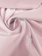 A close-up view of a light pink formal shirt featuring a button-down placket and smooth fabric.