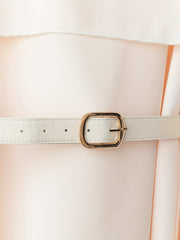 A close-up of an apricot-colored dress featuring a white belt with a gold buckle.
