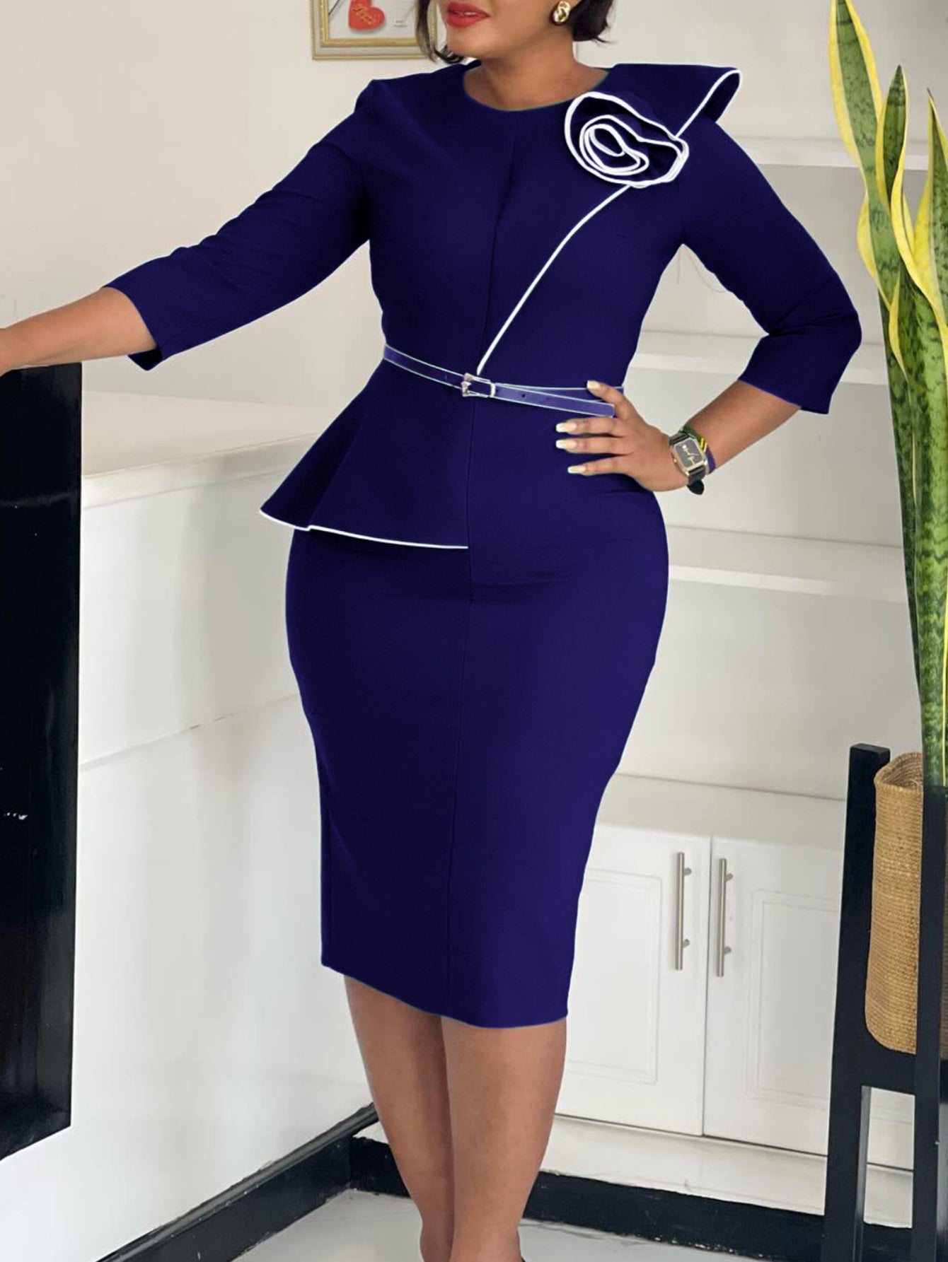 A dark blue bodycon dress with a peplum waist, white trim, and a decorative floral shoulder accent.