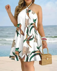 A woman wears a white mini halter dress featuring a tropical floral print against a beach backdrop.