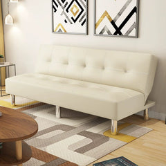 A beige tufted leather sofa bed with chrome legs sits on a patterned rug in a modern room.