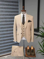 A three-piece khaki suit featuring a peak lapel blazer, vest, and trousers with olive loafers.