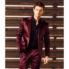 A man wears a slim-fit, single-breasted burgundy satin suit with a black button-down shirt.