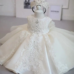 A sleeveless white formal baby dress with lace embroidery, bead embellishments, and a tiara.