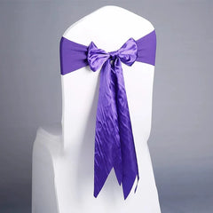 A white chair is decorated with a vibrant purple satin ribbon tied in a bow on the back.