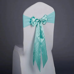 A white chair cover decorated with a shiny light blue satin ribbon tied in a bow.