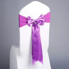 A white chair cover decorated with a vibrant purple satin ribbon tied in a bow on the back.