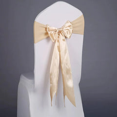 A white chair cover decorated with a champagne-colored satin ribbon tied in a bow.