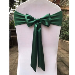 A white chair is decorated with a dark green satin ribbon tied in a bow on the back.