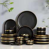 A set of black ceramic dinnerware featuring round plates and bowls with elegant gold-rimmed edges.
