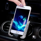 A smartphone held by a rhinestone-encrusted gravity car mount attached to an air vent.