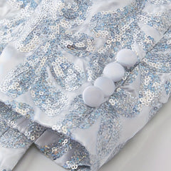 A close-up of a white blazer sleeve featuring silver floral sequins and four matching fabric buttons.