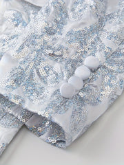 A close-up of a white sequined blazer sleeve featuring a floral pattern and four fabric buttons.