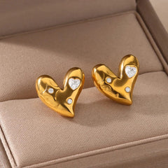 A pair of gold-colored stainless steel heart-shaped stud earrings accented with small zircon stones.