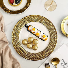 A white ceramic dinner plate with a wide, textured gold honeycomb rim holding a dessert and chocolates.