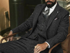 A man wearing a gray herringbone wool three-piece suit with a white shirt and patterned tie.