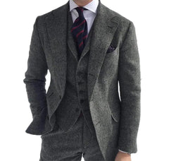 A man wears a gray herringbone wool three-piece suit with a white shirt and striped tie.