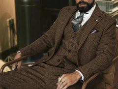 A man wears a brown herringbone wool three-piece suit with a white shirt and a gray tie.