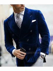 A man wears a blue velvet double-breasted blazer with a peak lapel, white shirt, and patterned tie.