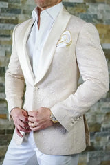 A man wears a cream-colored patterned tuxedo jacket with a white satin shawl lapel and white pants.