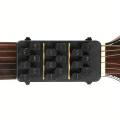 A black guitar chord learning device with numbered buttons attached to the neck of an acoustic guitar.